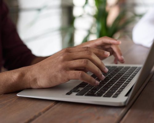 Hands of a person typing on a laptop keyboard indoors, ideal for remote work and freelancing themes.